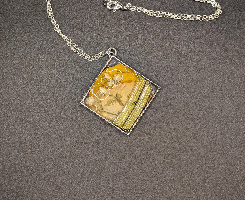 May include: Silver-toned necklace with a square pendant. The pendant features a yellow and beige resin design with dried plant elements and a silver frame. The chain is a delicate link style, perfect for everyday wear. __etsy:8301117701